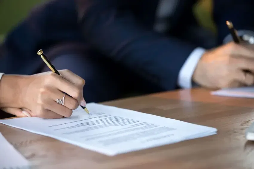 A man and woman signing a legal document at a table, representing the Burton Family Attorneys' professional services.