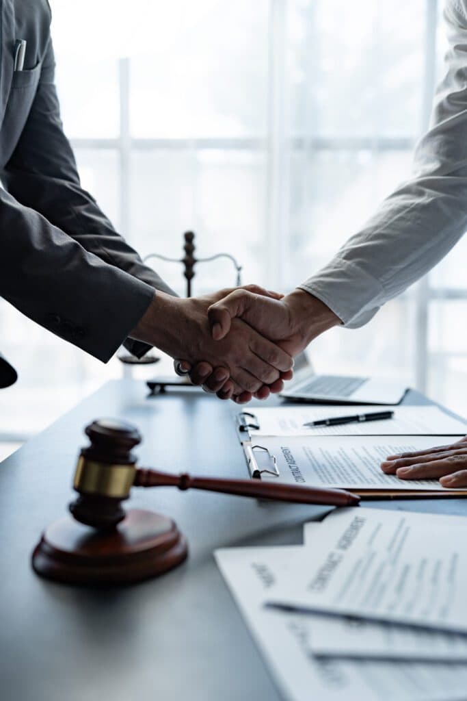 Business colleagues shaking hands at a desk with documents and a gavel, symbolizing collaboration at Burton Family Attorneys.