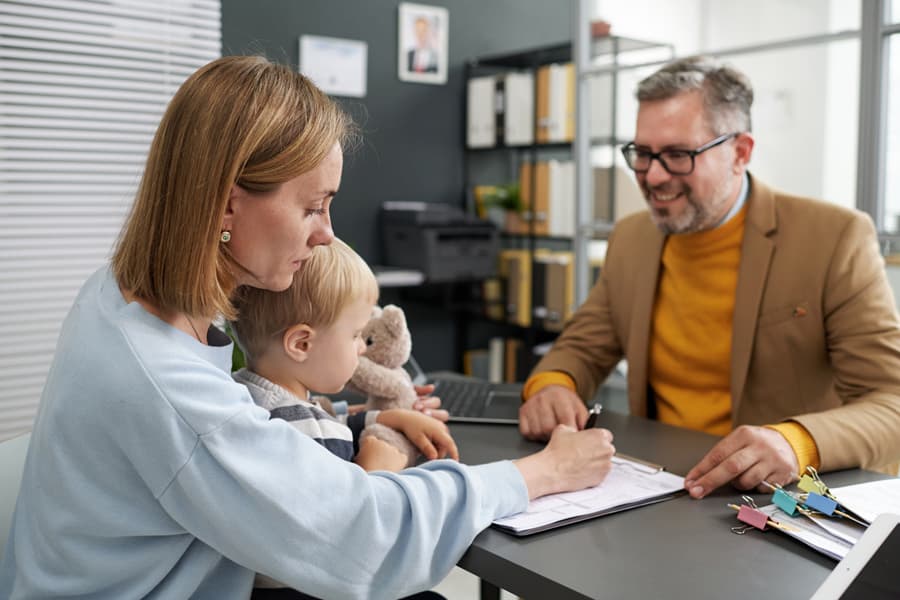A man and woman sit at a desk, engaged in conversation, while a child plays nearby, creating a warm family atmosphere.