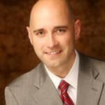 A professional portrait of Kenneth Burton, a bald man in formal attire, ready for a photo.
