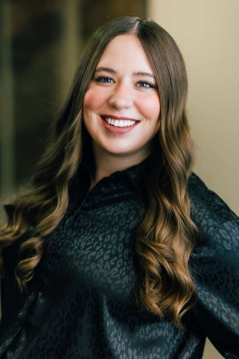 Portrait of OLIVIA GRAZIANO, a woman with long curly hair and a black shirt smiling at the camera