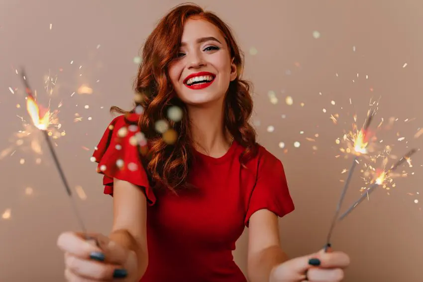 A woman in a red dress joyfully holds sparklers, symbolizing celebration and warmth, with the Burton Family Attorneys logo in view.