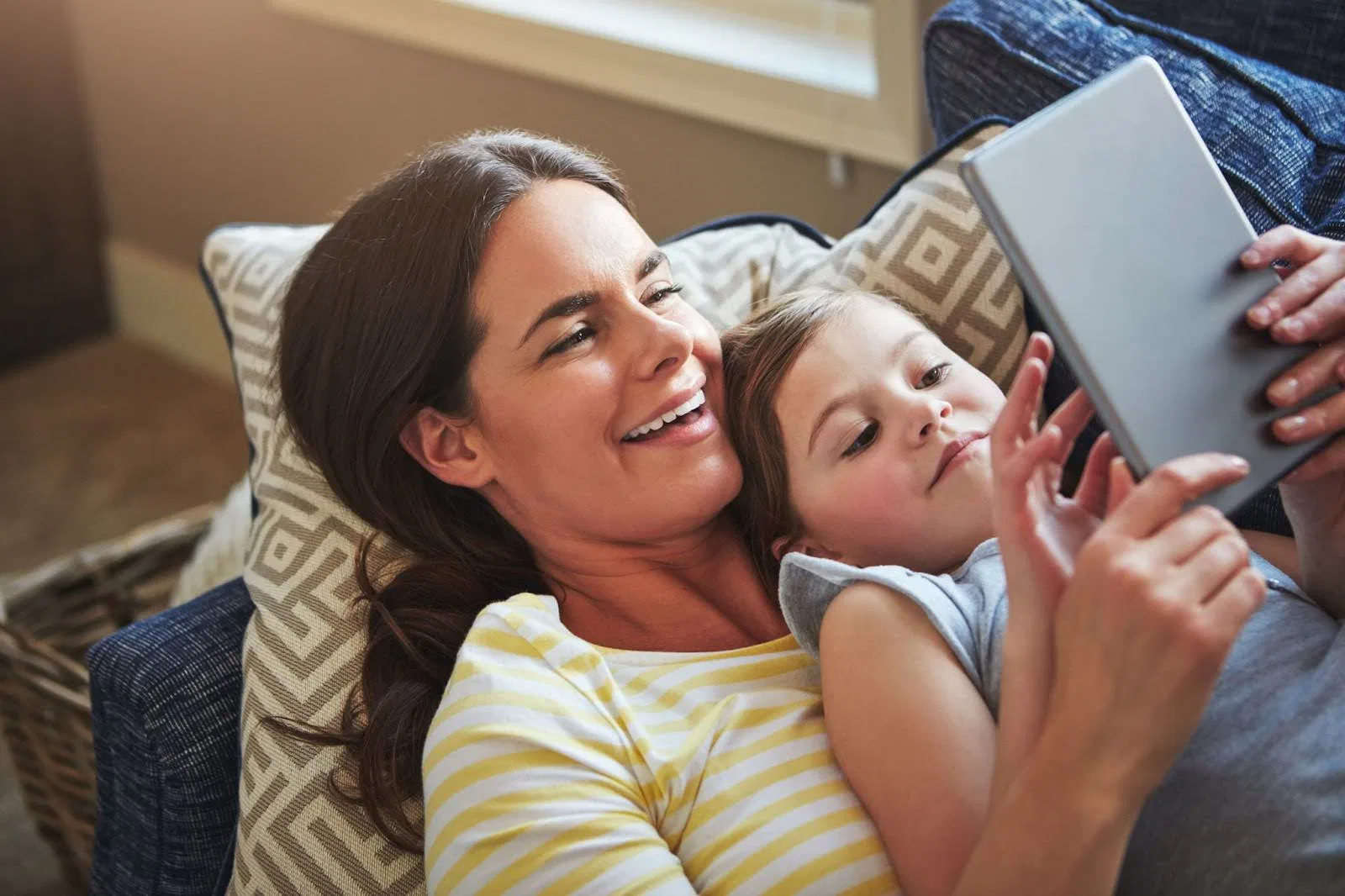 A woman and child share a moment on a couch, engaged with a tablet