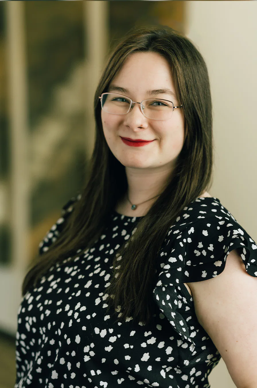 A woman wearing glasses and a polka dot dress, smiling and standing confidently.