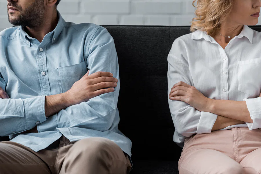 A man and woman with crossed arms sit on a couch, representing the Burton Family Attorneys' professional approach.