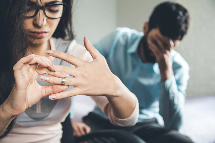 A woman touches her ring while a man sits on the couch, representing a moment of reflection at Burton Family Attorneys.