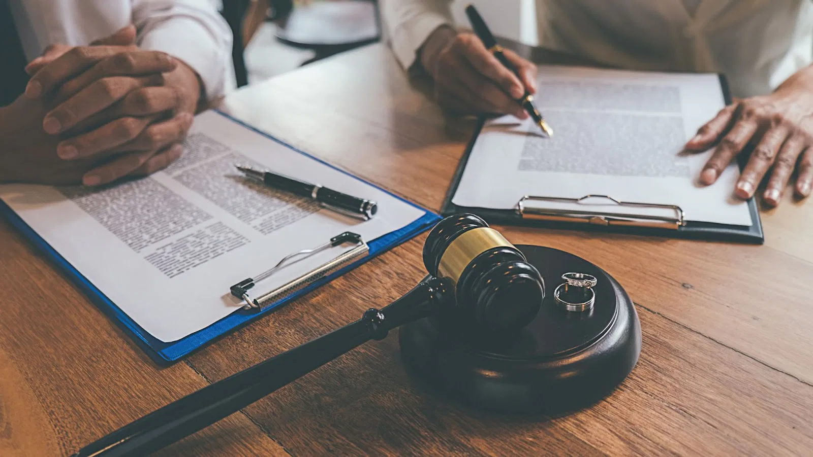 Couple signing divorce papers with judge's gavel and wedding rings on table, representing divorce settlement and family law proceedings